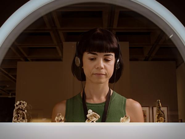 A woman wearing headphones listening to the Japan Supernatural audio guide at Art Gallery of New South Wales. She is looking at miniature Japanese sculptures.