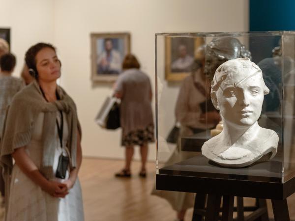 A woman wearing headphones is looking at a sculpture of a bust at the Josh Russell exhibition at the Art Gallery of NSW. She has an iPod Touch device on a lanyard and is listening to an audio guide