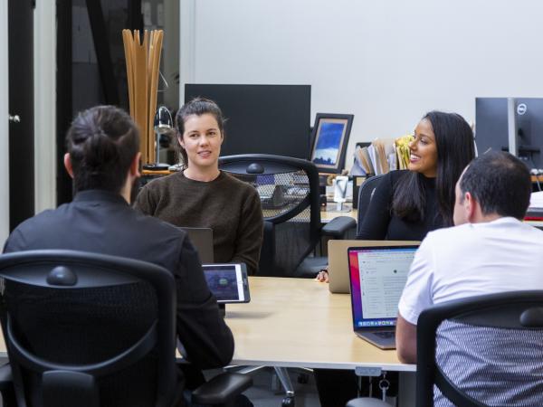 Four people sitting and having a discussion around a table, each with laptops
