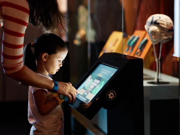 A mother and daughter stand in front of a touchscreen at the Australian Sports Museum