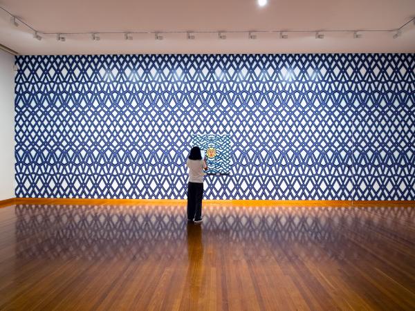 A woman stands in front of Josh Muir's artwork at the Bendigo Art Gallery. She is holding an iPad up to the artwork to trigger an augmented reality experience