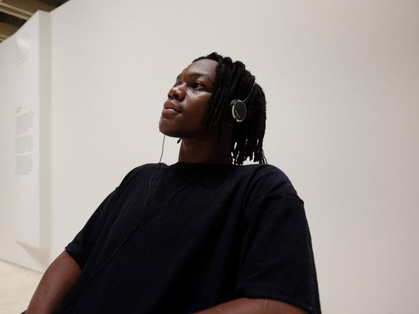 A young man wearing a black t-shirt wearing headphones listens to the Matisse: Life & Spirit audio experience at the Art Gallery of NSW.