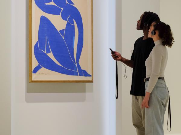 A young man and young woman with audio guides and headphones look up at Matisse's Blue Nude II.
