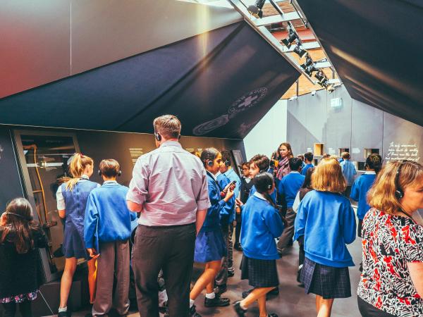 Interior of the Spirit of the ANZAC touring exhibition. There is a group of school children wearing headphones