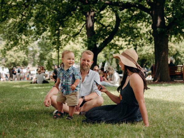 A family sits on Parliament House lawns in Hobart while waiting in a virtual queue to enter the Taste of Summer festival.
