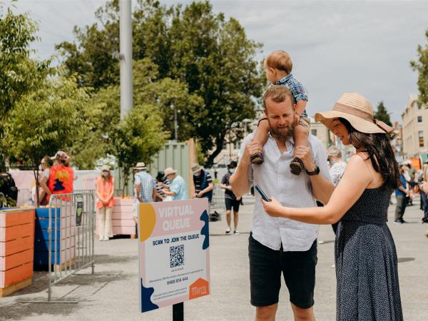 A woman with her family scans a QR code to join a virtual queue for the Taste of Summer festival.