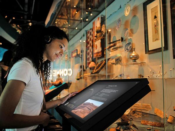 A young woman is reading information on a touch screen digital label at the Western Australian museum Boola Bardip. She is standing in front of a glass showcase