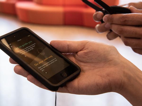 A person holding a mobile device displaying options for WA Museum Boola Bardip Gogo audio experience.