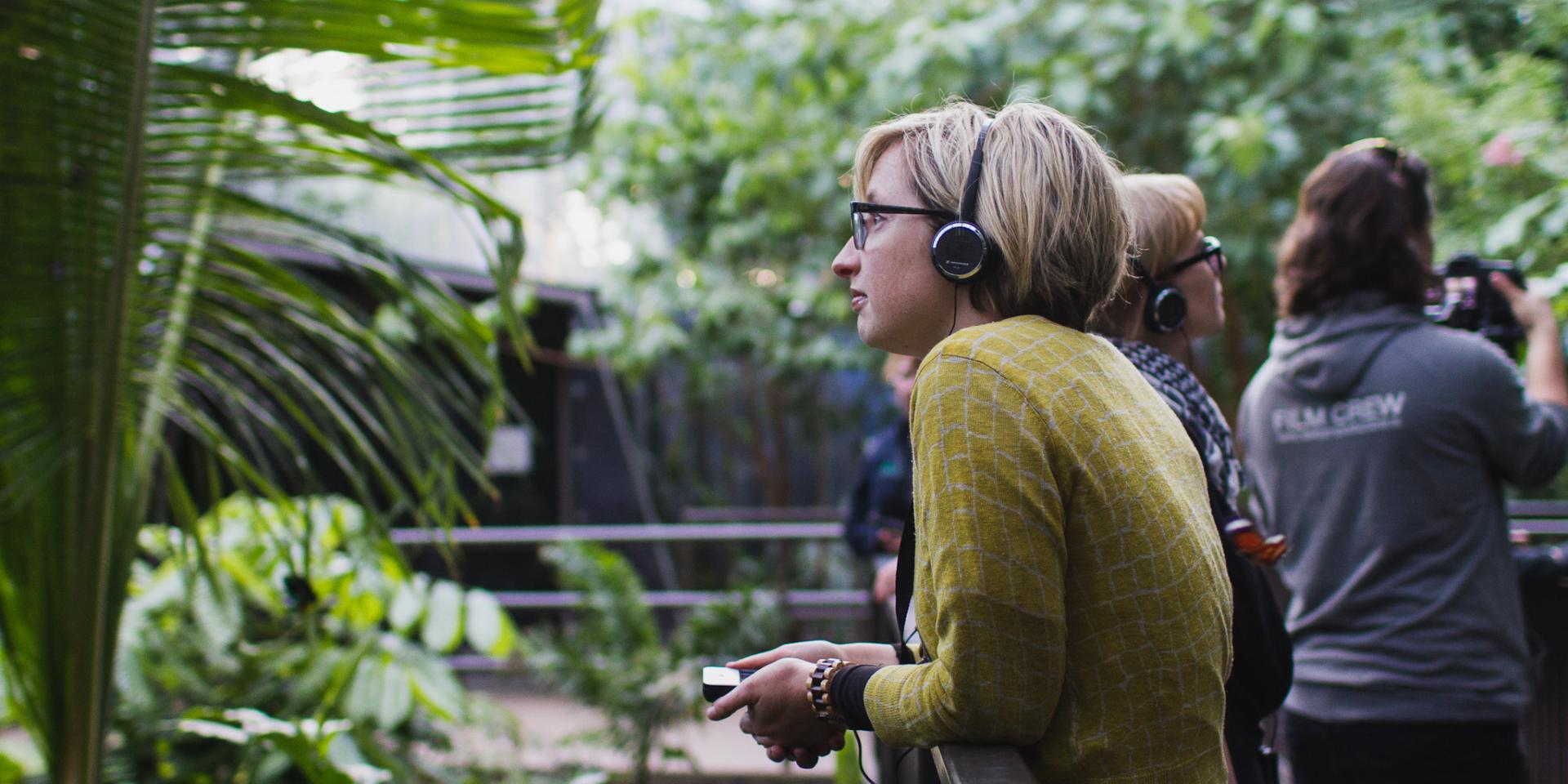 A young woman wearing headphones and holding an iPod Touch looks into an animal enclosure at Melbourne Zoo.
