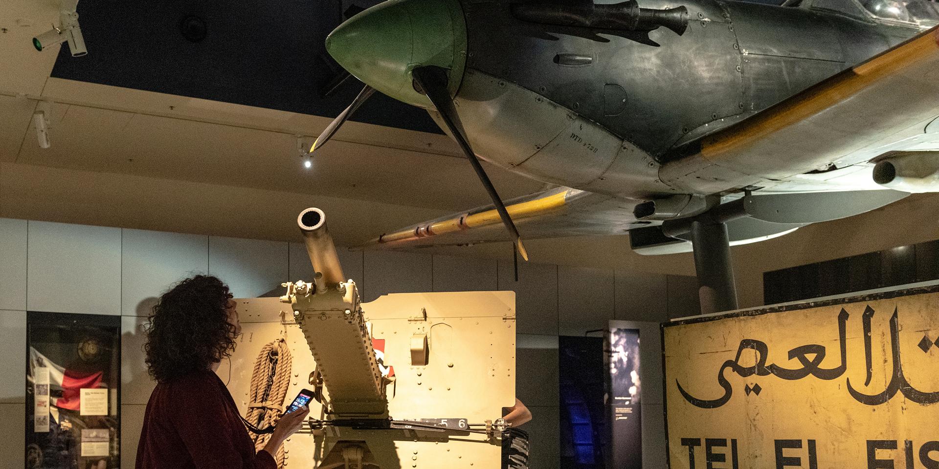 A woman holding an iPod touch looking up at a Airplane installation at the Australian War Memorial
