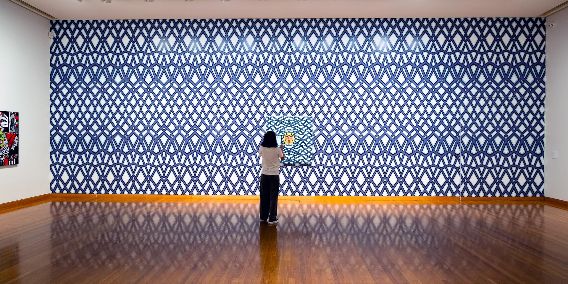 A woman stands in front of Josh Muir's artwork at the Bendigo Art Gallery. She is holding an iPad up to the artwork to trigger an augmented reality experience