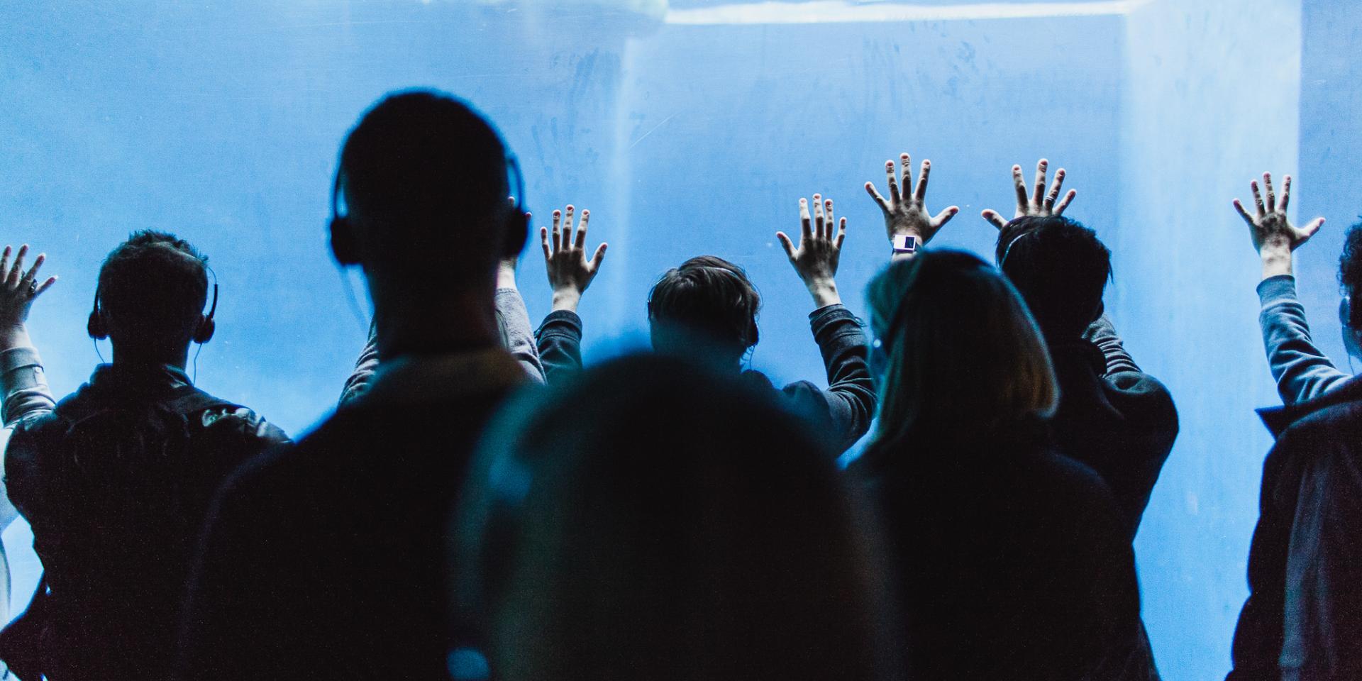 People wearing headphones put their hands up to the glass of a large aquarium.