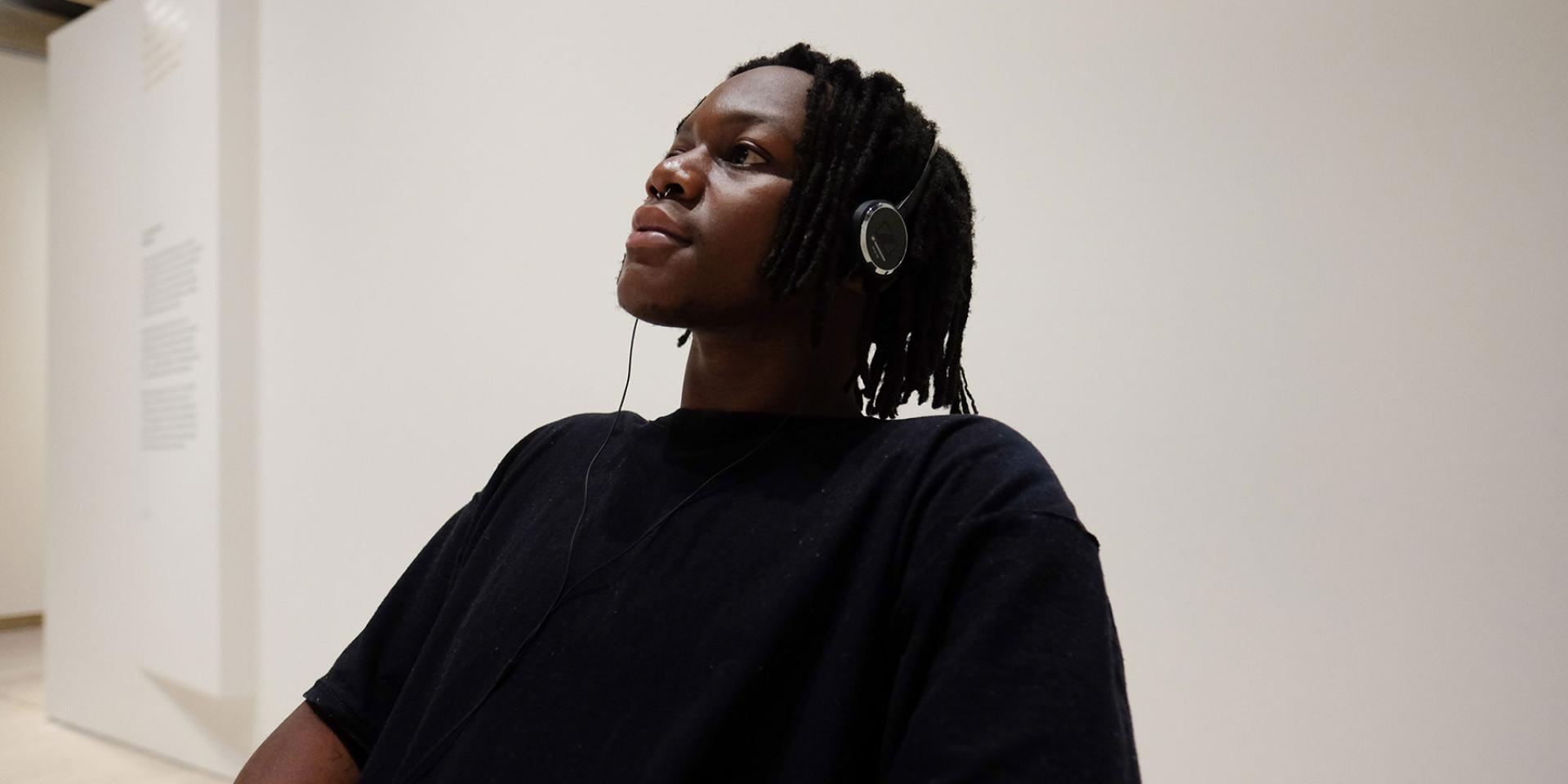 A young man wearing a black t-shirt wearing headphones listens to the Matisse: Life & Spirit audio experience at the Art Gallery of NSW.