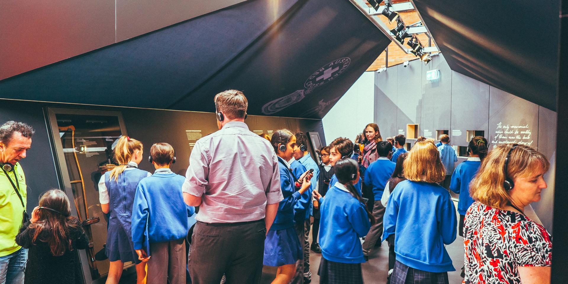 Interior of the Spirit of the ANZAC touring exhibition. There is a group of school children wearing headphones