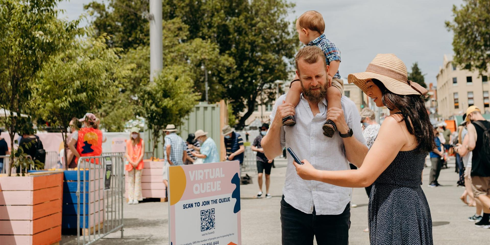 A woman with her family scans a QR code to join a virtual queue for the Taste of Summer festival.