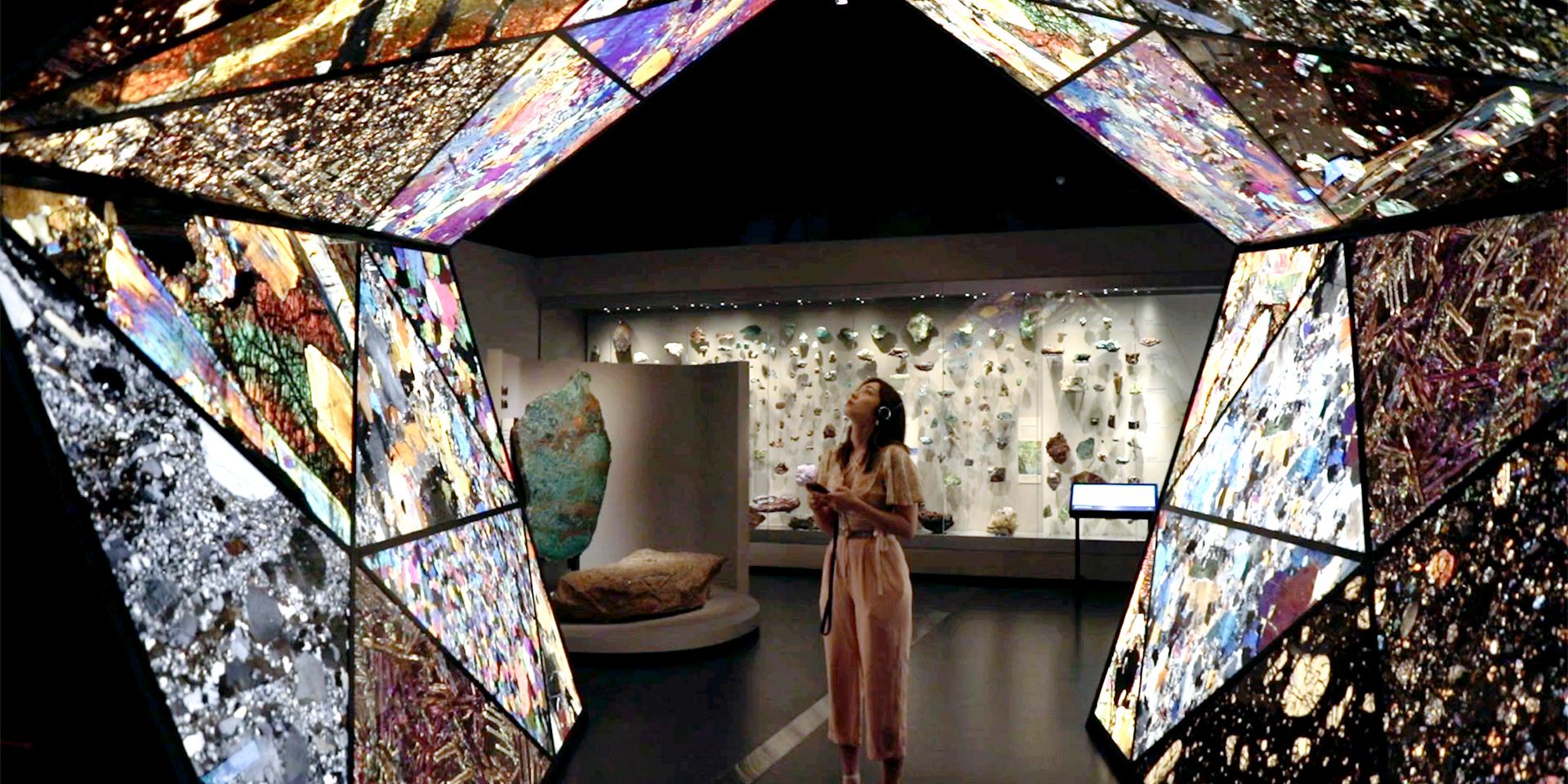 A woman is standing in a room at the Western Australian Museum Boola Bardip. She is looking up at the backlit ceiling and is wearing headphones listening to an audio guide
