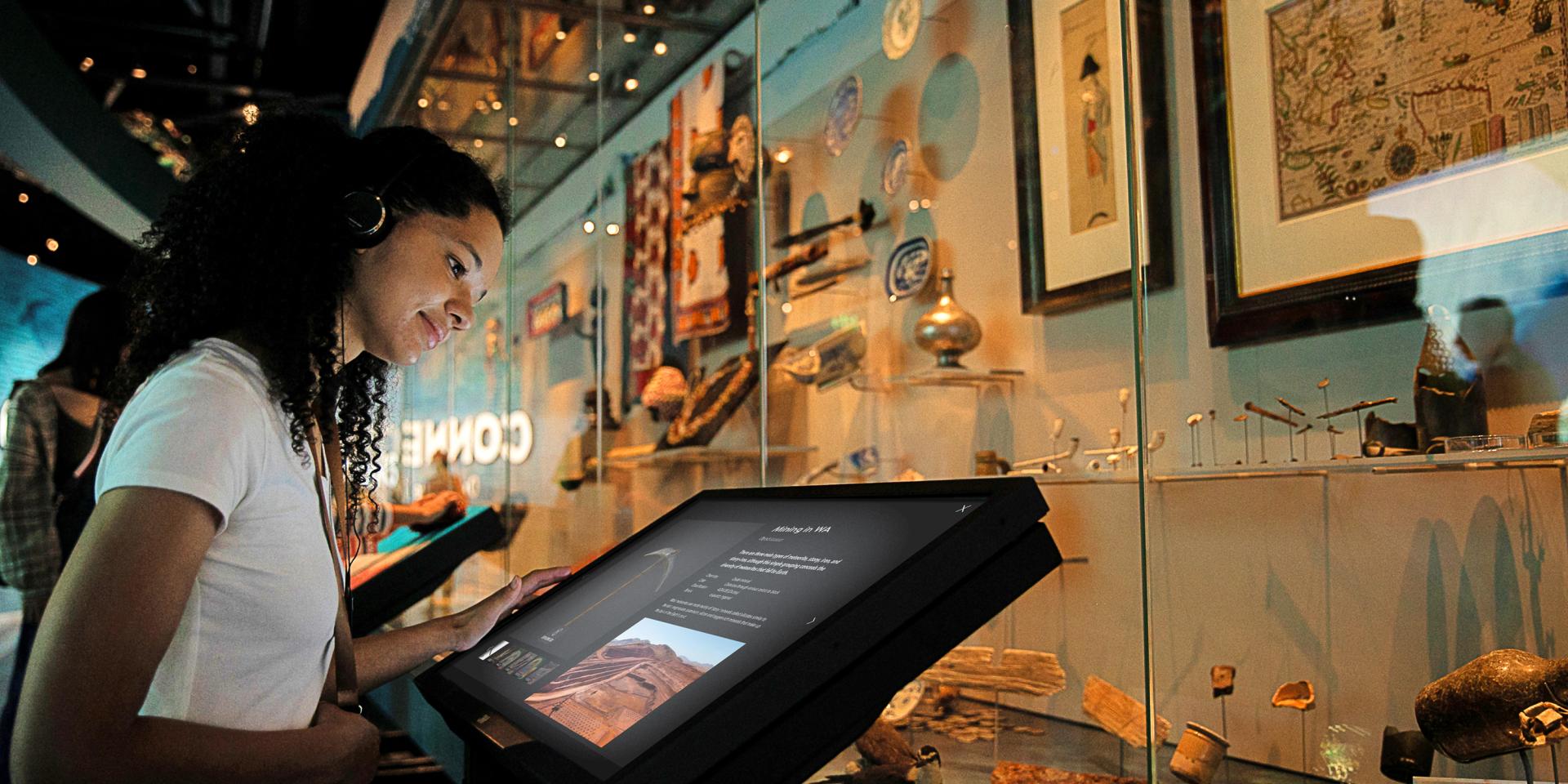 A young woman is reading information on a touch screen digital label at the Western Australian museum Boola Bardip. She is standing in front of a glass showcase