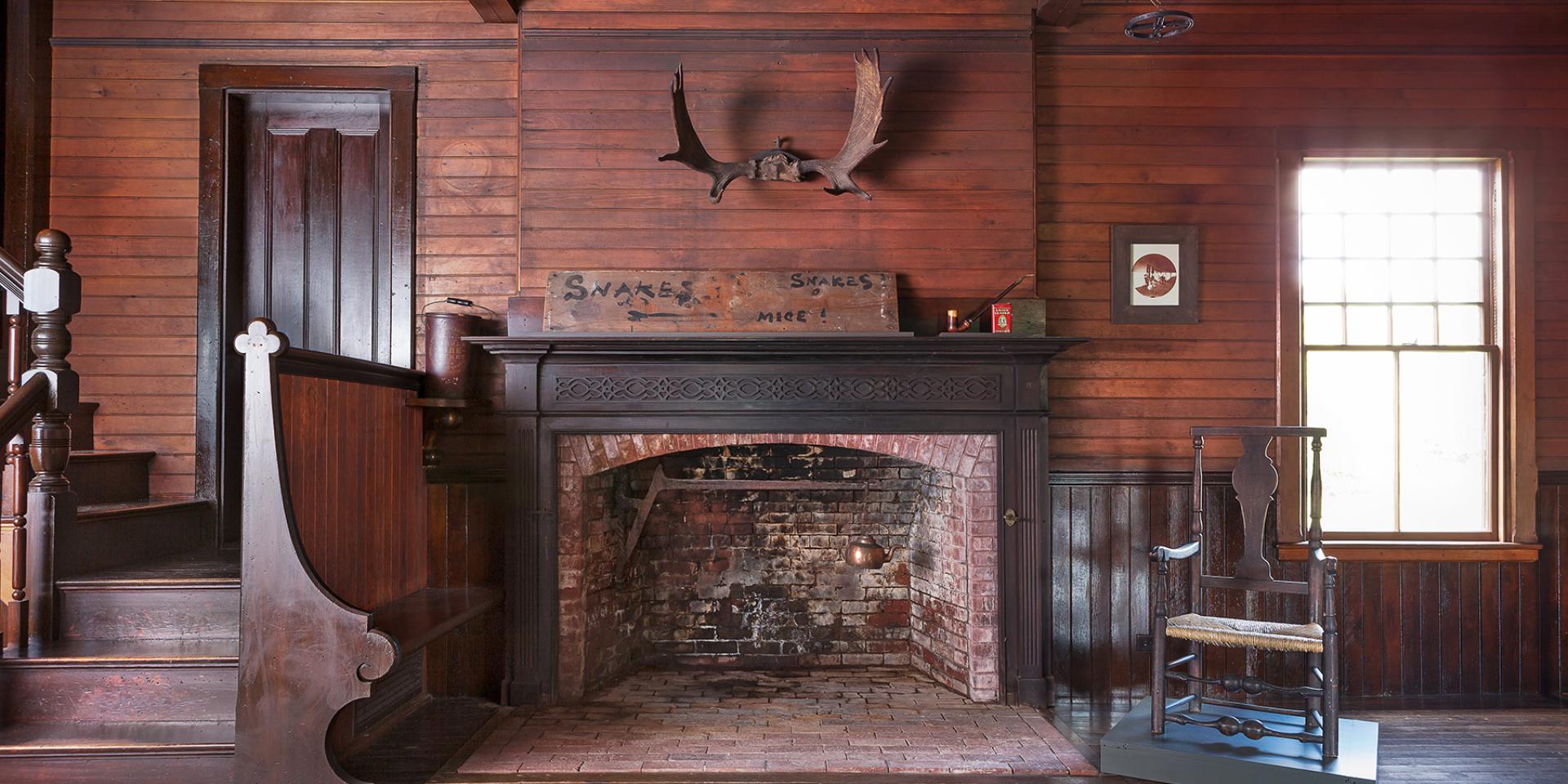 An empty, open fireplace below with deer antlers hanging on the wall above.
