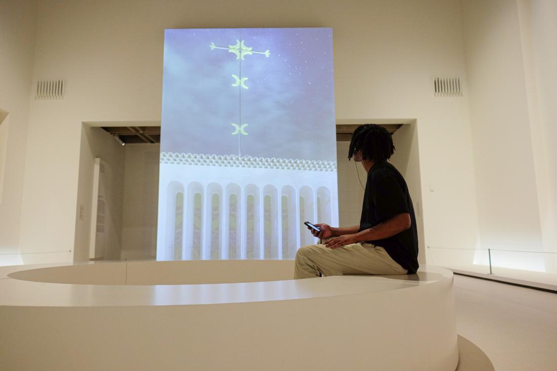 A young man looks up at an image of chapel while sitting and listening to the Matisse: Life and Spirit audio guide